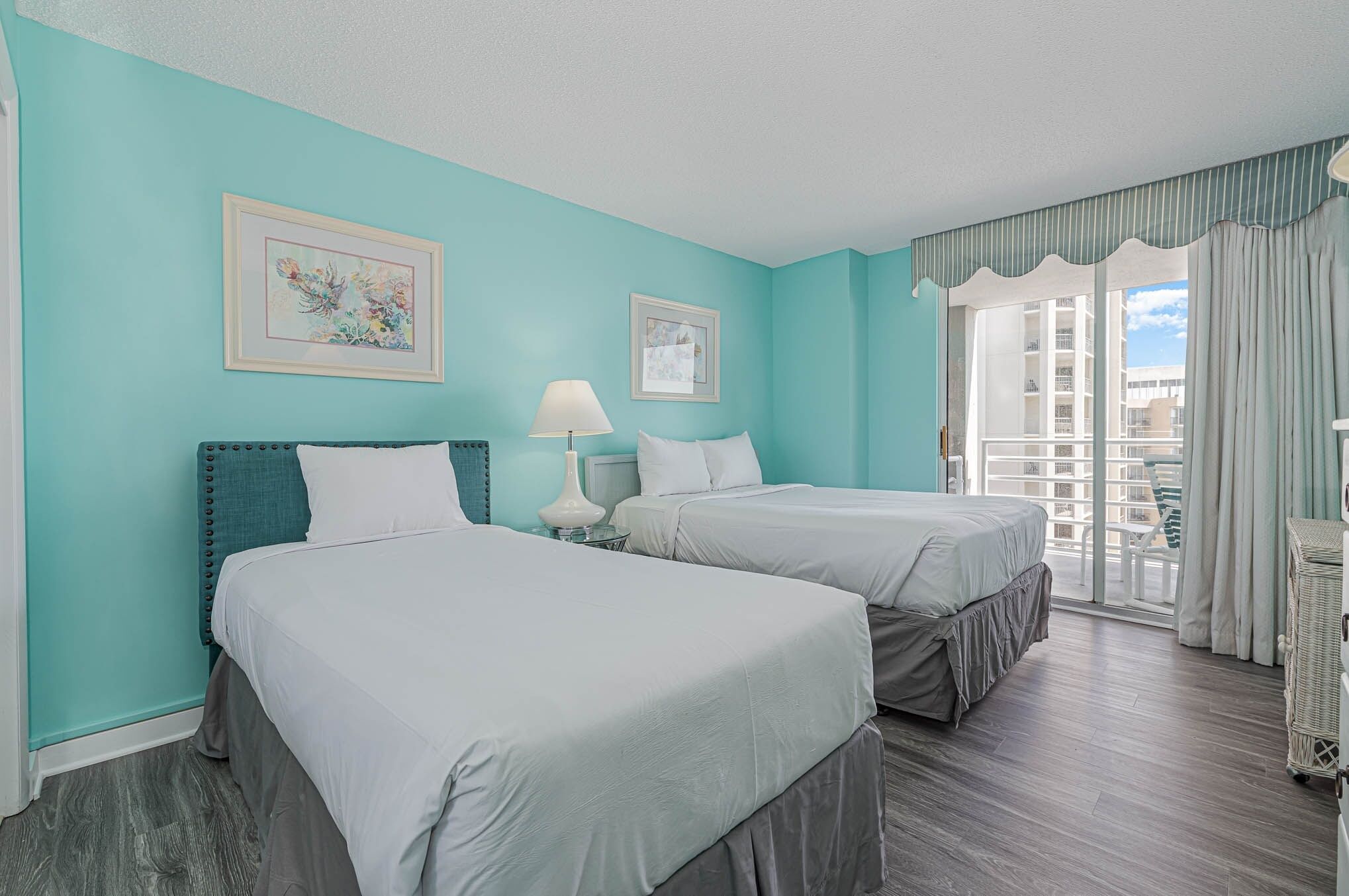A hotel room with two beds, teal walls, and a balcony with curtains.