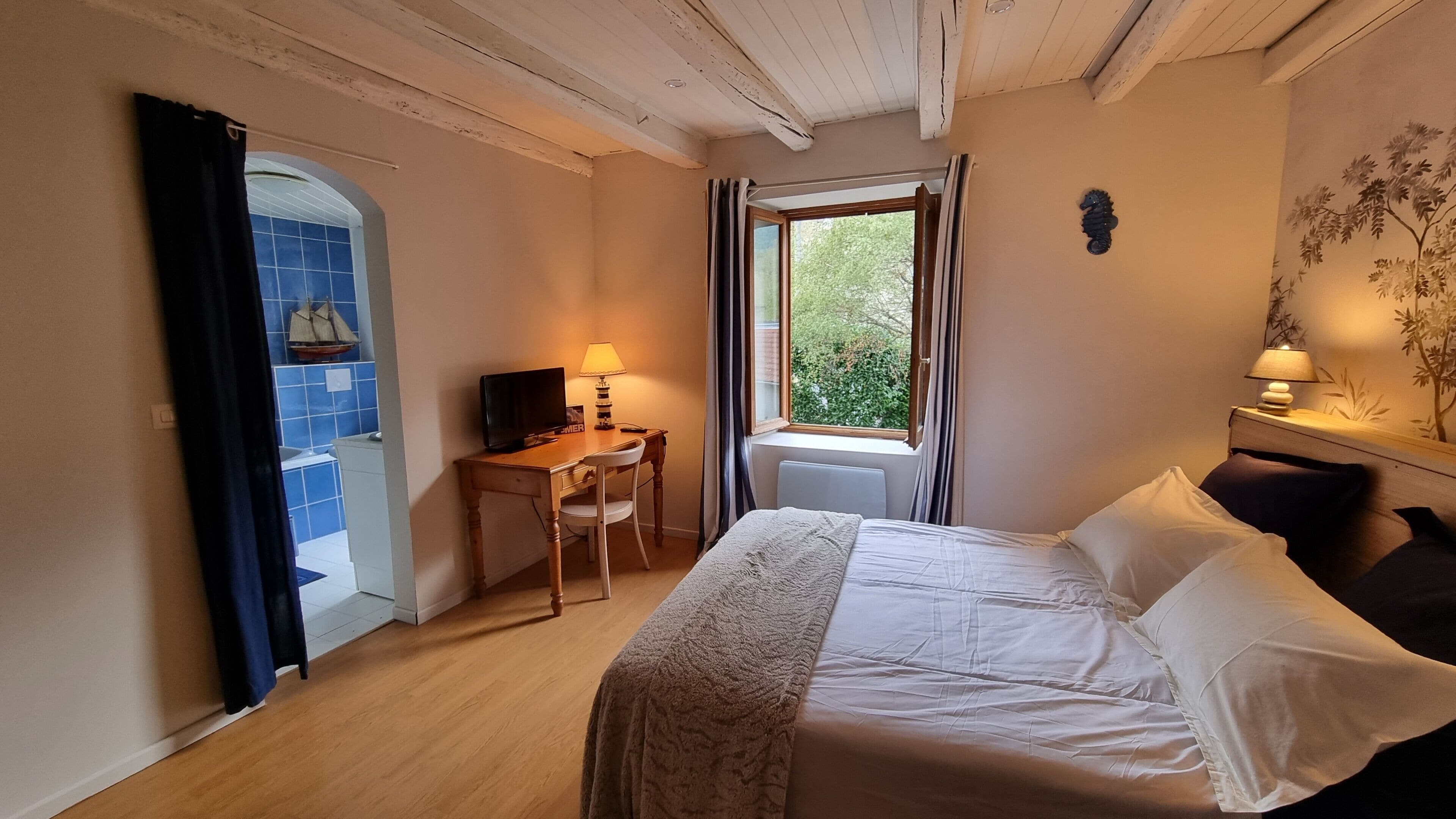 A bedroom with a bed, a desk with a chair, a TV, and a window with curtains.