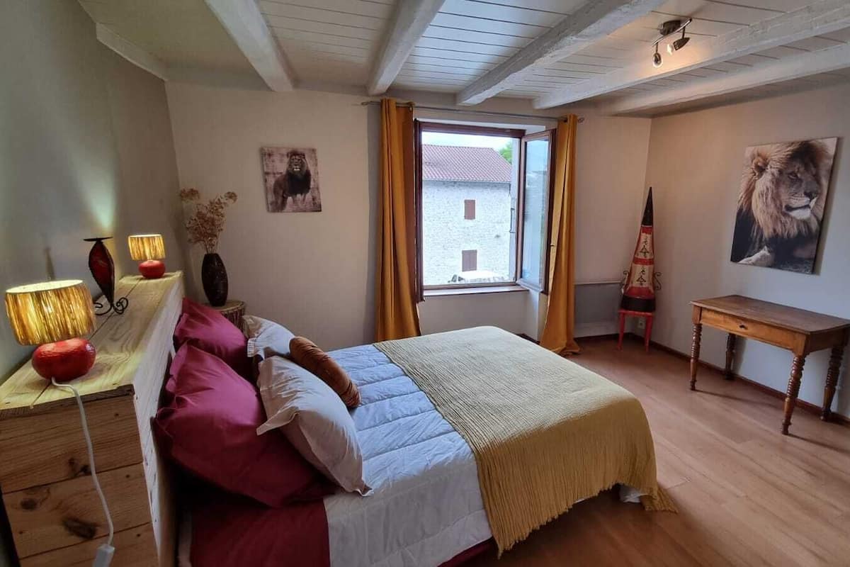 Un dormitorio con cama, lámparas de noche, una ventana, una silla y una mesa.