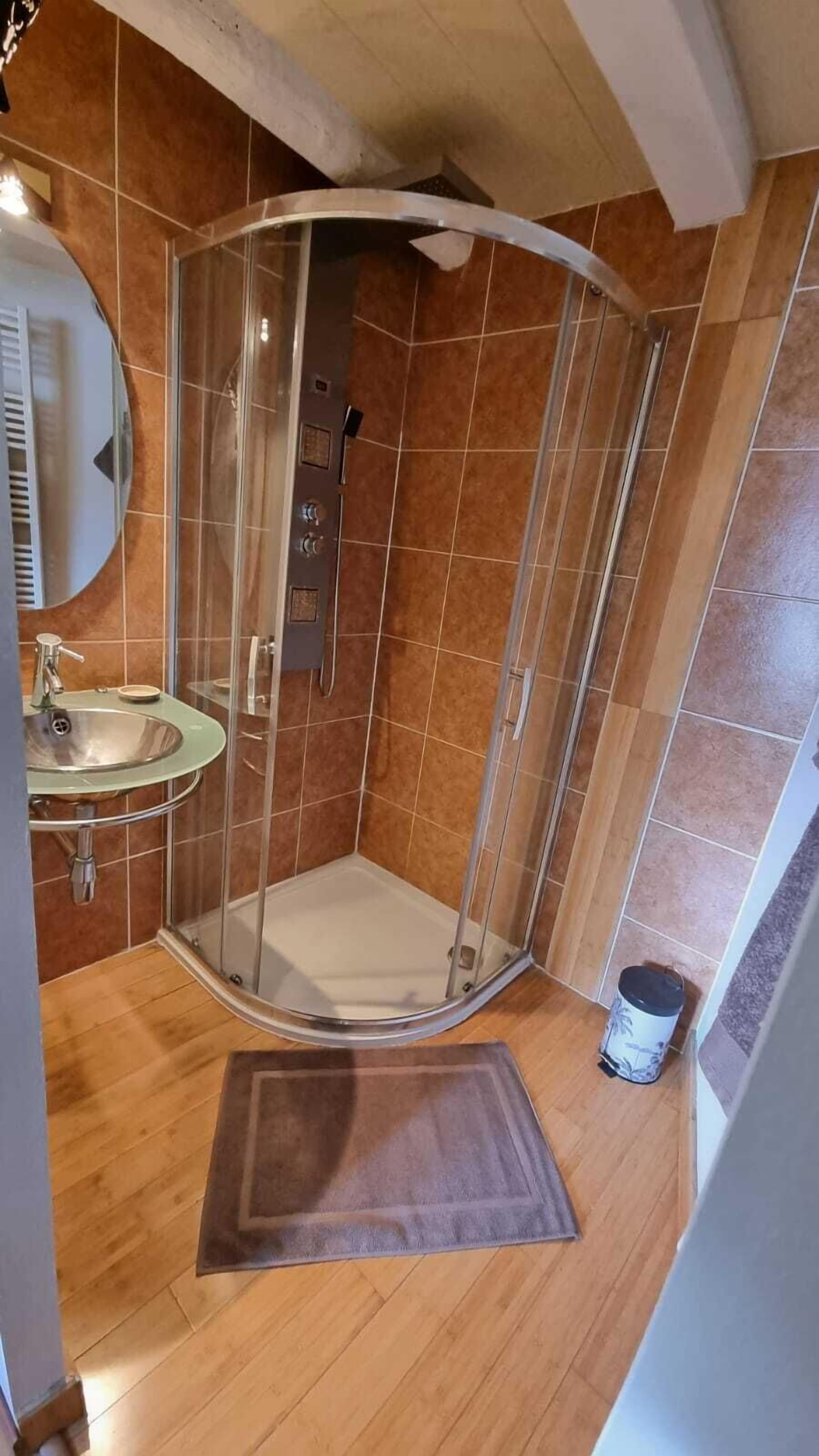 Un baño en esquina con cabina de ducha de vidrio, lavamanos y piso de madera.