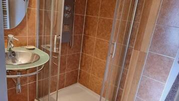 Un baño en esquina con cabina de ducha de vidrio, lavamanos y piso de madera.
