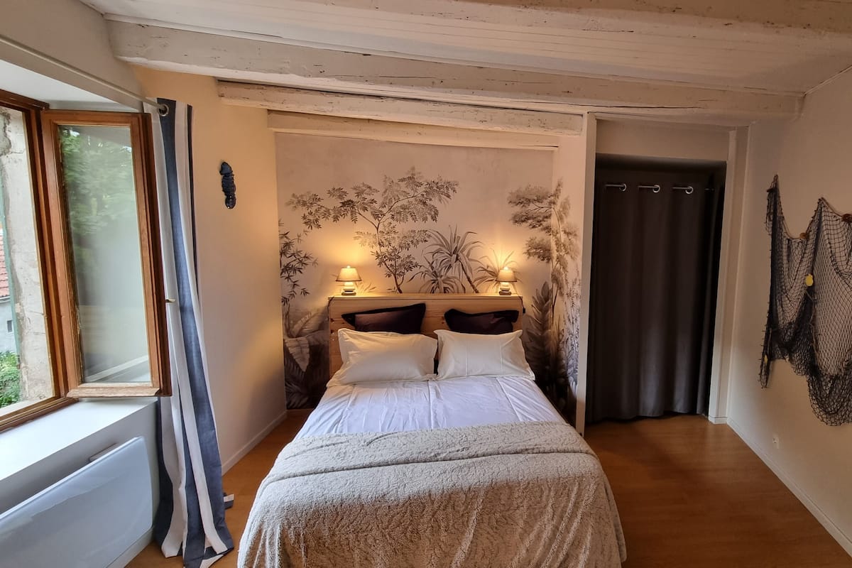 Un dormitorio con una cama, una ventana, un muro con un mural de plantas y una decoración de red.