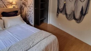 Un dormitorio con cama, mesita de noche, lámpara, estante en la pared y un ventanal grande.