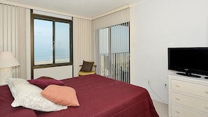 A hotel room with a bed, a television, a chair, and a view of the sea through large windows. - Bonaire 404 2 Bedroom Condo by RedAwning (Ocean City)