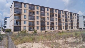 A multi-story residential building with balconies, a sandy ground level, and a clear sky. - Bonaire 404 2 Bedroom Condo by RedAwning (Ocean City)