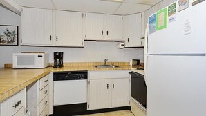 A compact kitchen with white cabinets, a microwave, a coffee maker, a dishwasher, and a refrigerator. - Bonaire 404 2 Bedroom Condo by RedAwning (Ocean City)