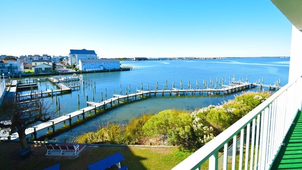 A waterfront view with a dock extending into the water, surrounded by greenery and residential buildings. - Thunder Island 157d 2 Bedroom Condo by RedAwning (Ocean City)