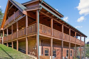A two-story wooden cabin with a balcony on the upper floor, a covered porch, and a view of the surrounding landscape. - Peace Of Mind 3 Bedroom Cabin by RedAwning (Sevierville)