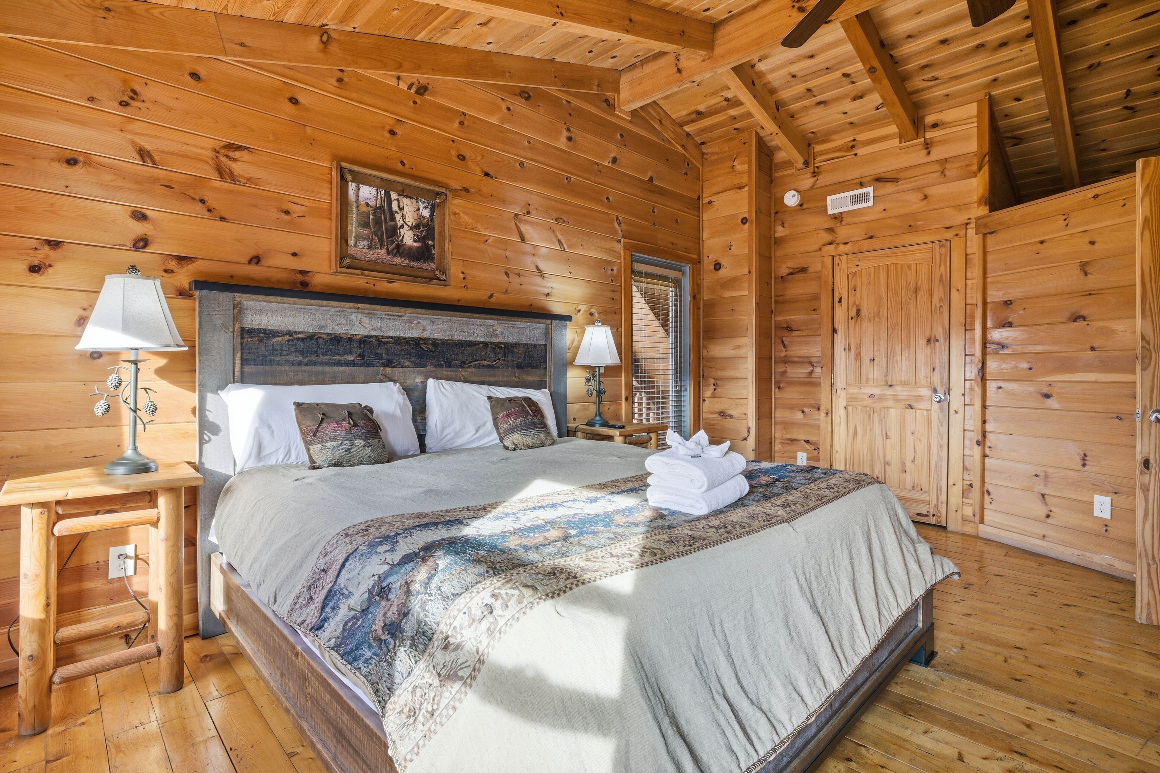Une chambre à coucher dans un chalet en bois, comprenant un lit, deux tables de chevet, une petite table, une lampe, un tableau et une armoire.
