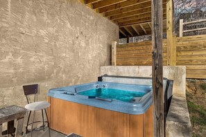 A hot tub with a wooden deck and a chair, set against a stone wall. - Peace Of Mind 3 Bedroom Cabin by RedAwning (Sevierville)