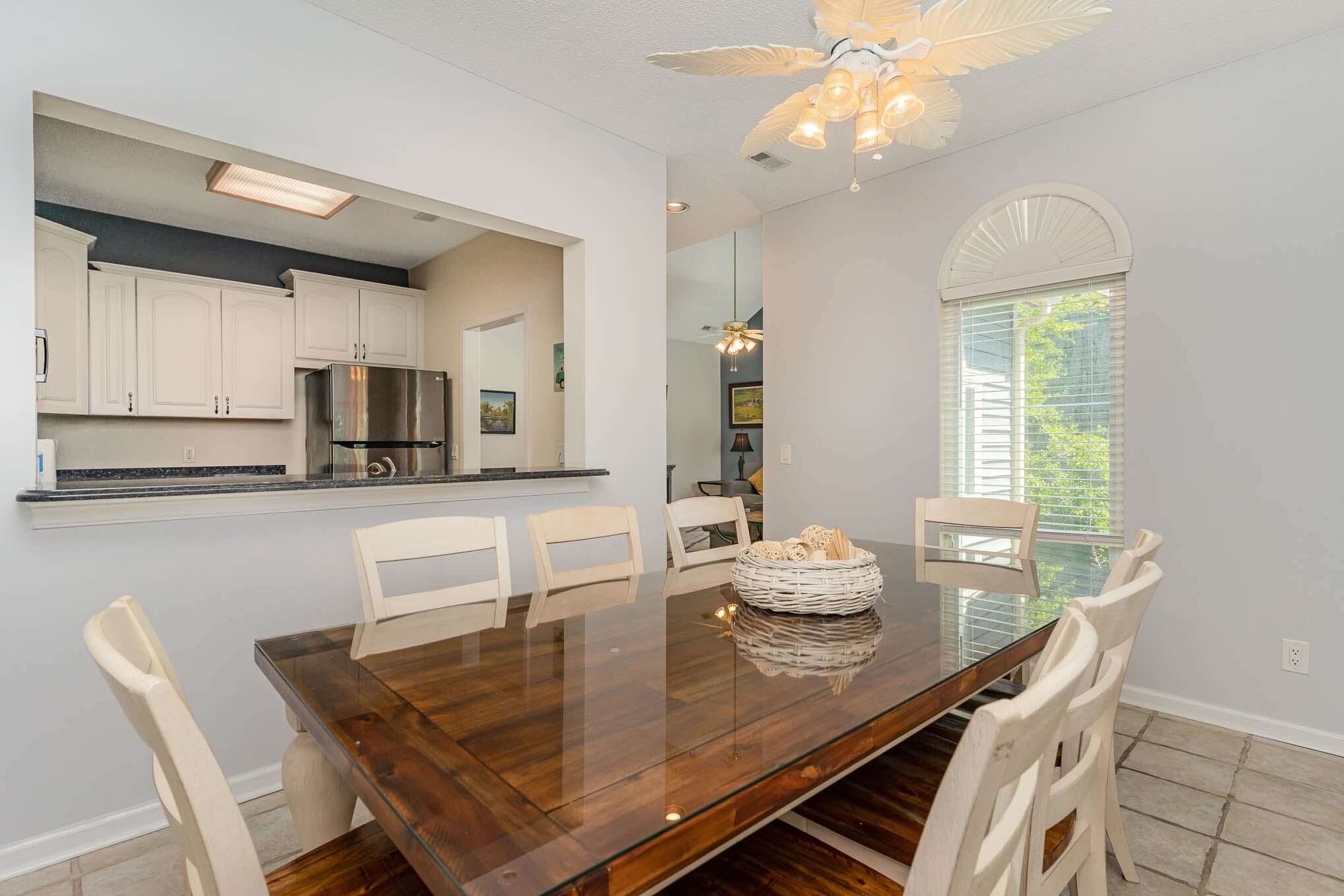 A modern kitchen with white cabinets, a stainless steel refrigerator, and a dining area with a wooden table and white chairs.