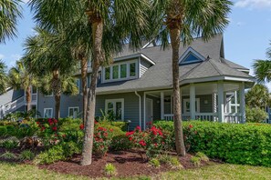 A two-story house with a porch, surrounded by palm trees and red flowering plants. - Gorgeous and spacious 4 bedroom villa - 8D Windermere by the Sea 4 Villa (Myrtle Beach)