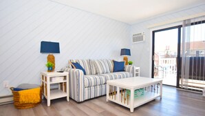 A modern living room with a striped sofa, two side tables, a white coffee table, and a wicker basket. - Harbour Bay 34 2 Bedroom Townhouse by RedAwning (Ocean City)
