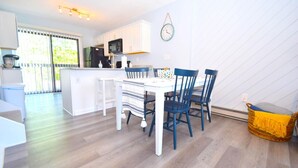 A modern kitchen with white cabinets, a central island, and a dining area with a striped tablecloth and blue chairs. - Harbour Bay 34 2 Bedroom Townhouse by RedAwning (Ocean City)