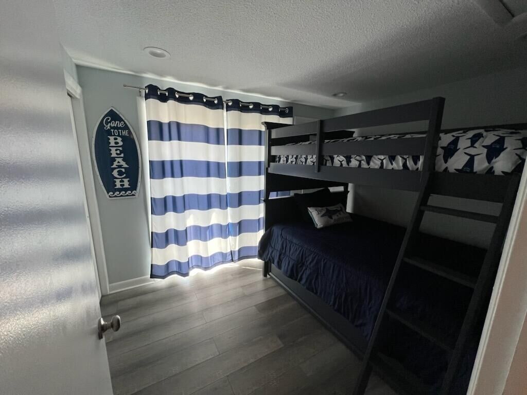 Une chambre avec des lits superposés, des rideaux à rayures et un panneau décoratif sur le mur.