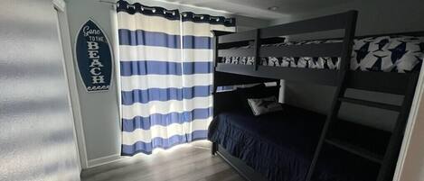Une chambre avec des lits superposés, des rideaux à rayures et un panneau décoratif sur le mur.