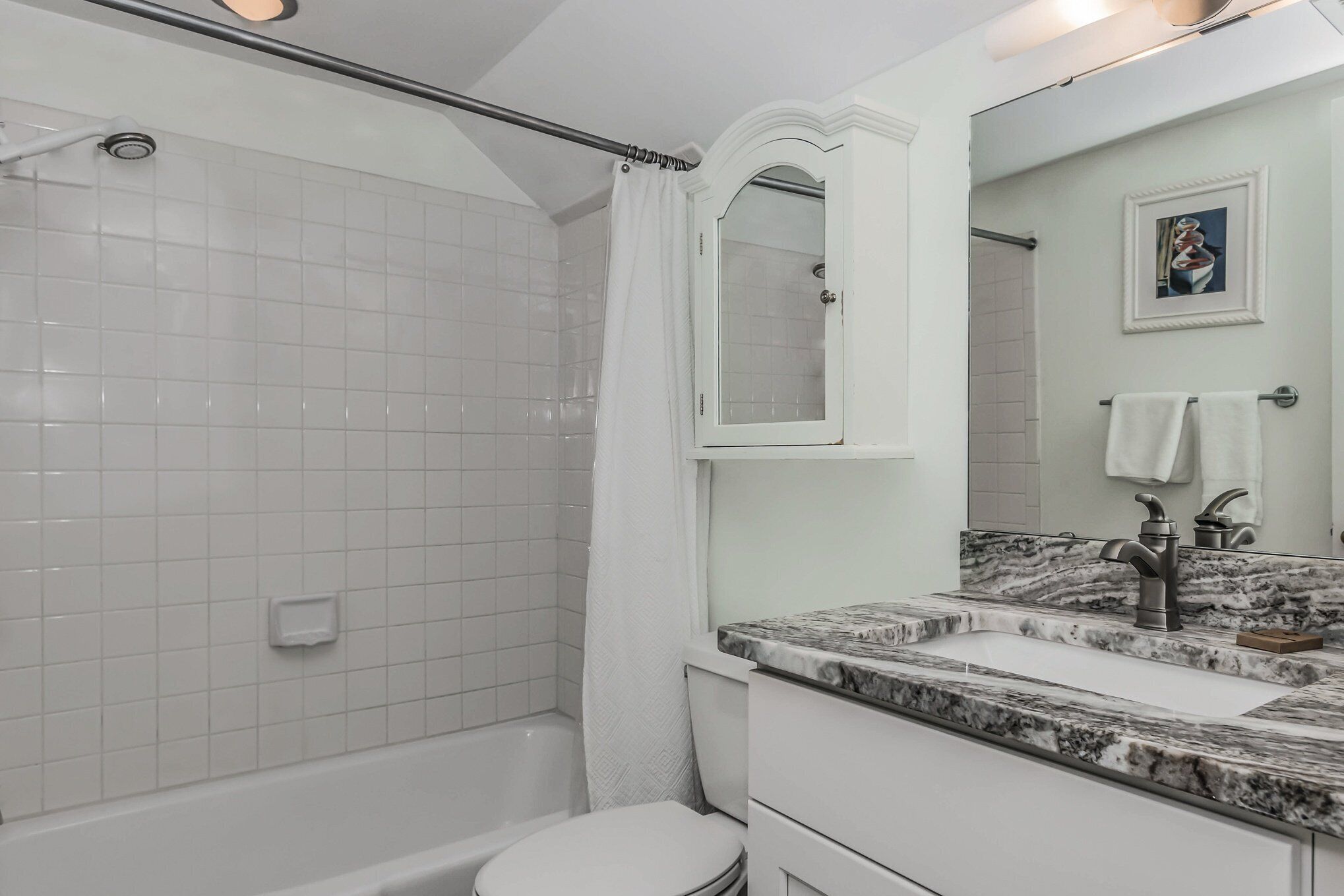 A bathroom with a shower, toilet, and sink with a marble countertop.