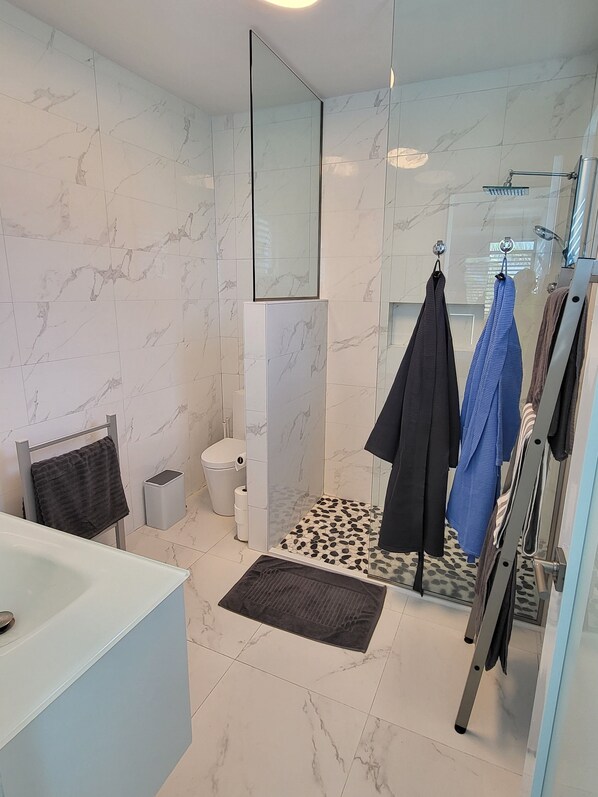 A modern bathroom with a marble floor, a glass shower enclosure, a toilet, and a sink.