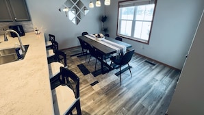 Une cuisine moderne dotée d’un évier encastré, d’un coin repas avec une table et des chaises en bois, et d’une grande fenêtre qui laisse entrer la lumière naturelle.