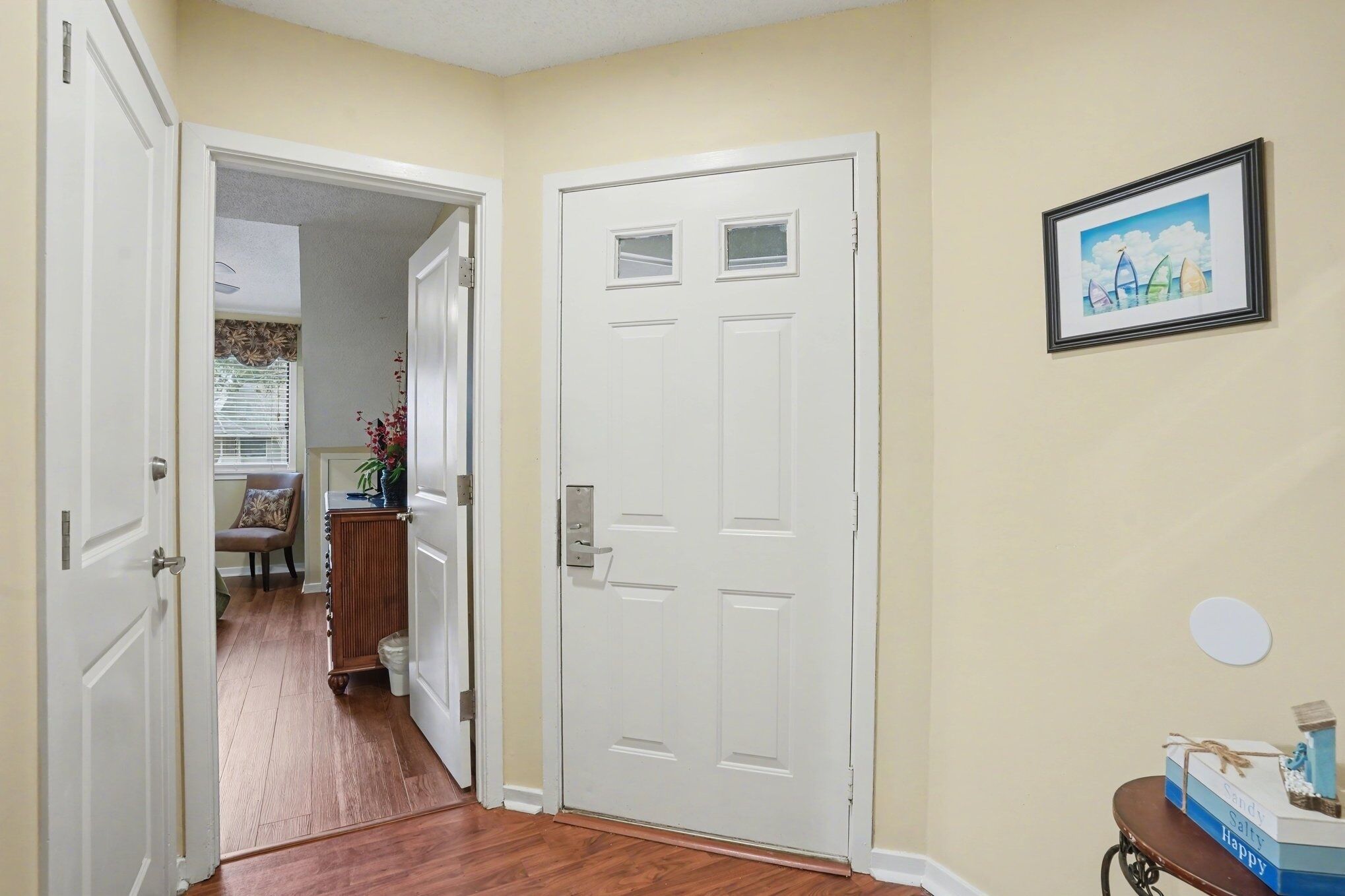 A hallway with a white door, a framed picture on the wall, and a small table with a box.