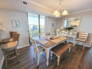 Uma sala de jantar com mesa de madeira, cadeiras e vista para o exterior.