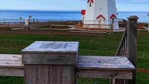 A lighthouse with a white and red exterior, situated on a grassy area with a wooden bench in the foreground.