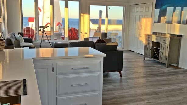 A spacious living area with a large white island, a dining table, and a view of the ocean.