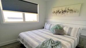 A bedroom with a bed, a window, a headboard, and a wall-mounted artwork.