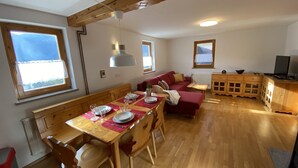 A dining area with wooden furniture, a red sofa, and a kitchen area with wooden cabinets and a television. - Quiet Family sized House in a small village (Radovljica)