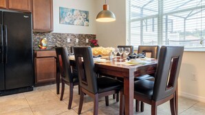 A dining area with a wooden table, black chairs, and a hanging pendant light. - Luxury 4 bedroom 3 bath pool Home 283 (Kissimmee)