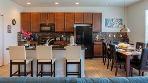 A modern kitchen with wooden cabinets, a central island with bar stools, a dining area with a table and chairs, and a kitchen island with a sink and microwave. - Luxury 4 bedroom 3 bath pool Home 283 (Kissimmee)