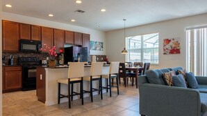 A modern kitchen with wooden cabinets, a built-in microwave, and a central island with bar stools. - Luxury 4 bedroom 3 bath pool Home 283 (Kissimmee)