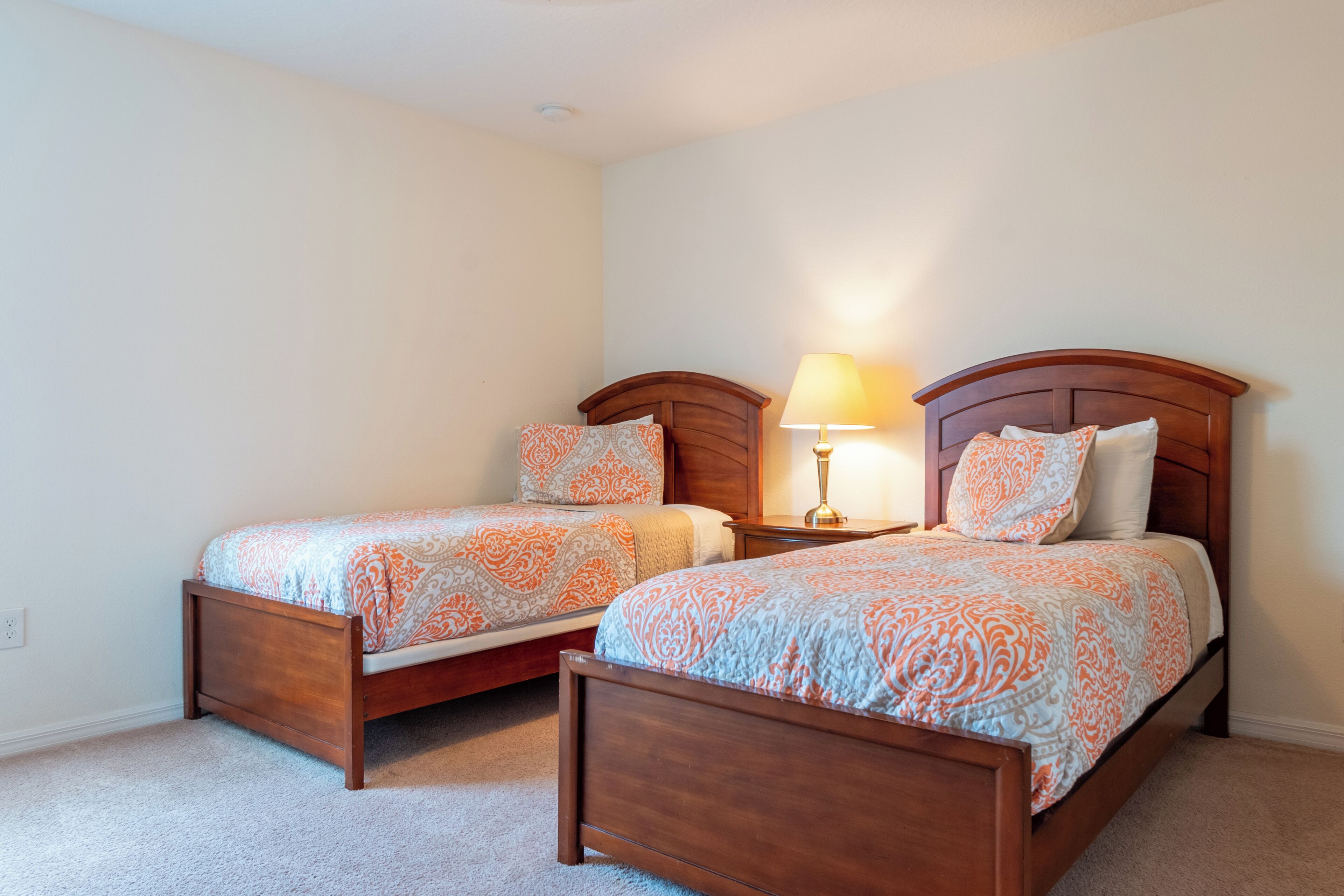 Une chambre à coucher avec deux lits simples, chacun doté d’une tête de lit en bois, d’une table de chevet avec une lampe et d’une couvre-lit à motifs.