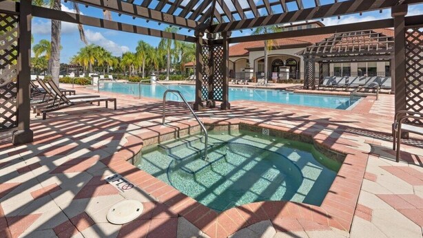 A pool area with a hot tub, lounge chairs, and a pergola structure. - Luxury 4 bedroom 3 bath pool Home 283 (Kissimmee)