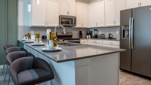 Cozinha moderna com armários brancos, eletrodomésticos de aço inoxidável e uma ilha central com banquetas.