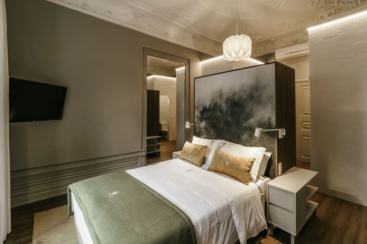 A modern bedroom with a large bed, a flat-screen TV, a nightstand, and a painting on the wall.