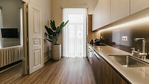 A modern kitchen with a wooden floor, stainless steel appliances, and a large potted plant.