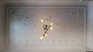 Plafond met ingewikkelde bloem- en geometrische patronen, een moderne kroonluchter met zichtbare lampen en een ingebouwd plafondpaneel.