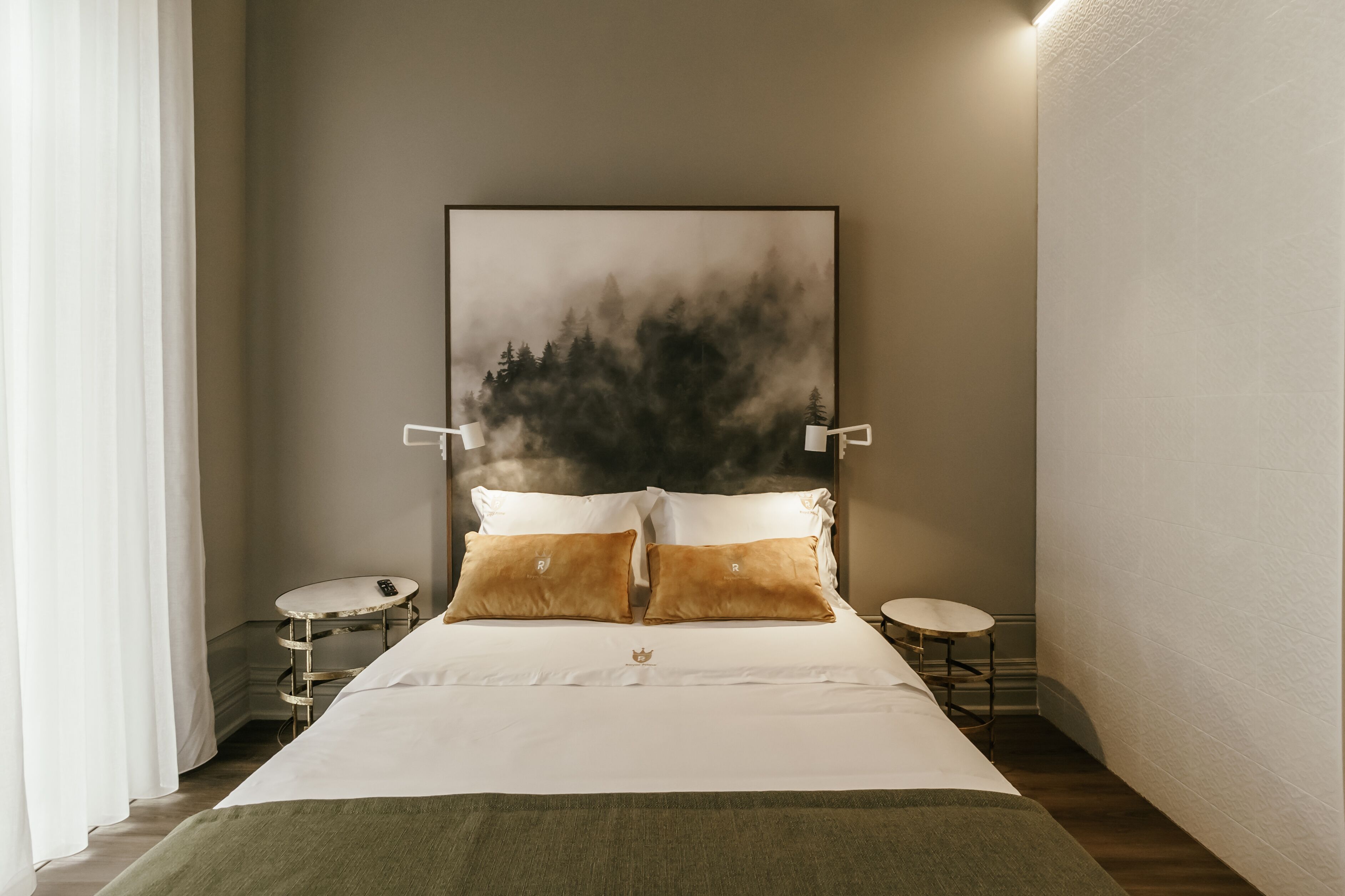 A neatly arranged bedroom with a large bed, two bedside tables, and a wall-mounted artwork depicting a forest scene.