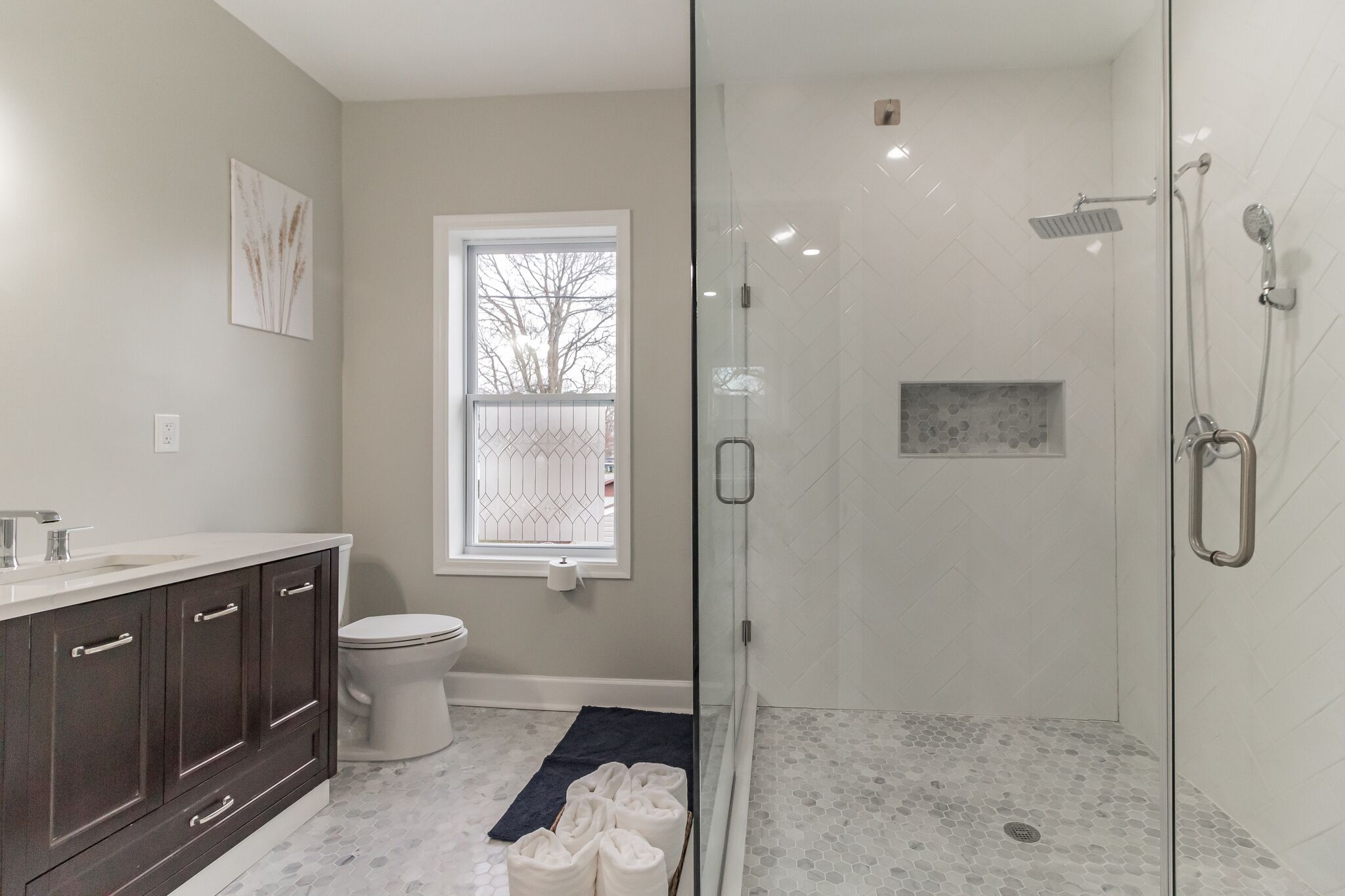 Een moderne badkamer met een douchecabine van glas, een toilet en een wastafelmeubel met donkere kastjes.