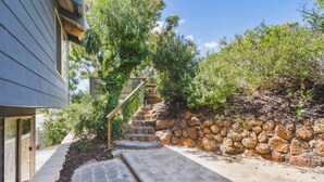 A stone staircase leading up to a wooden deck, surrounded by greenery and a stone wall.