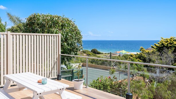 A balcony with a white table, a potted plant, and a view of the ocean.
