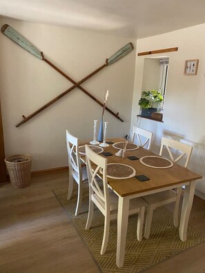 A dining area with a wooden table, white chairs, and a woven rug. There are two candlesticks on the table.