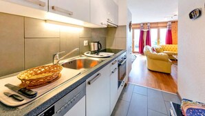 A modern kitchen with a large island, a dining area with a yellow sofa, and a view of the living room through an open door. - Chalet, wifi, 200m from resort center, view mountain, balcony, fireplace or stove, tv, ski locker (Les Collons)