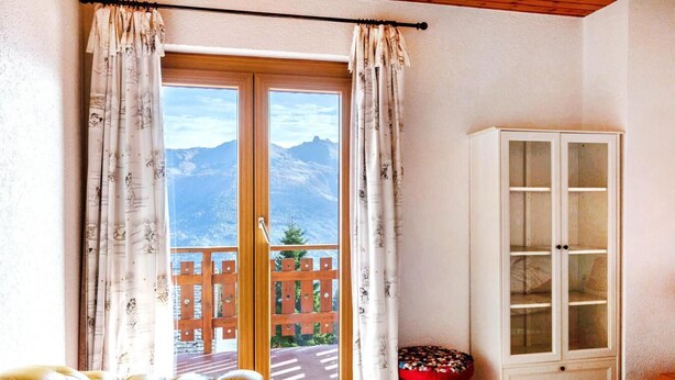 A room with a large sliding glass door, a yellow tufted sofa, a red ottoman, and a white cabinet. - Chalet, wifi, 200m from resort center, view mountain, balcony, fireplace or stove, tv, ski locker (Les Collons)