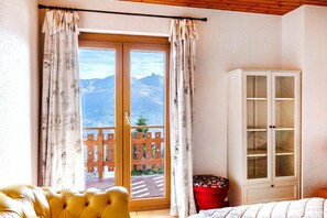 Una habitació amb una gran porta corredissa de vidre, un sofà groc amb borla, un otomà vermell i un armari blanc.