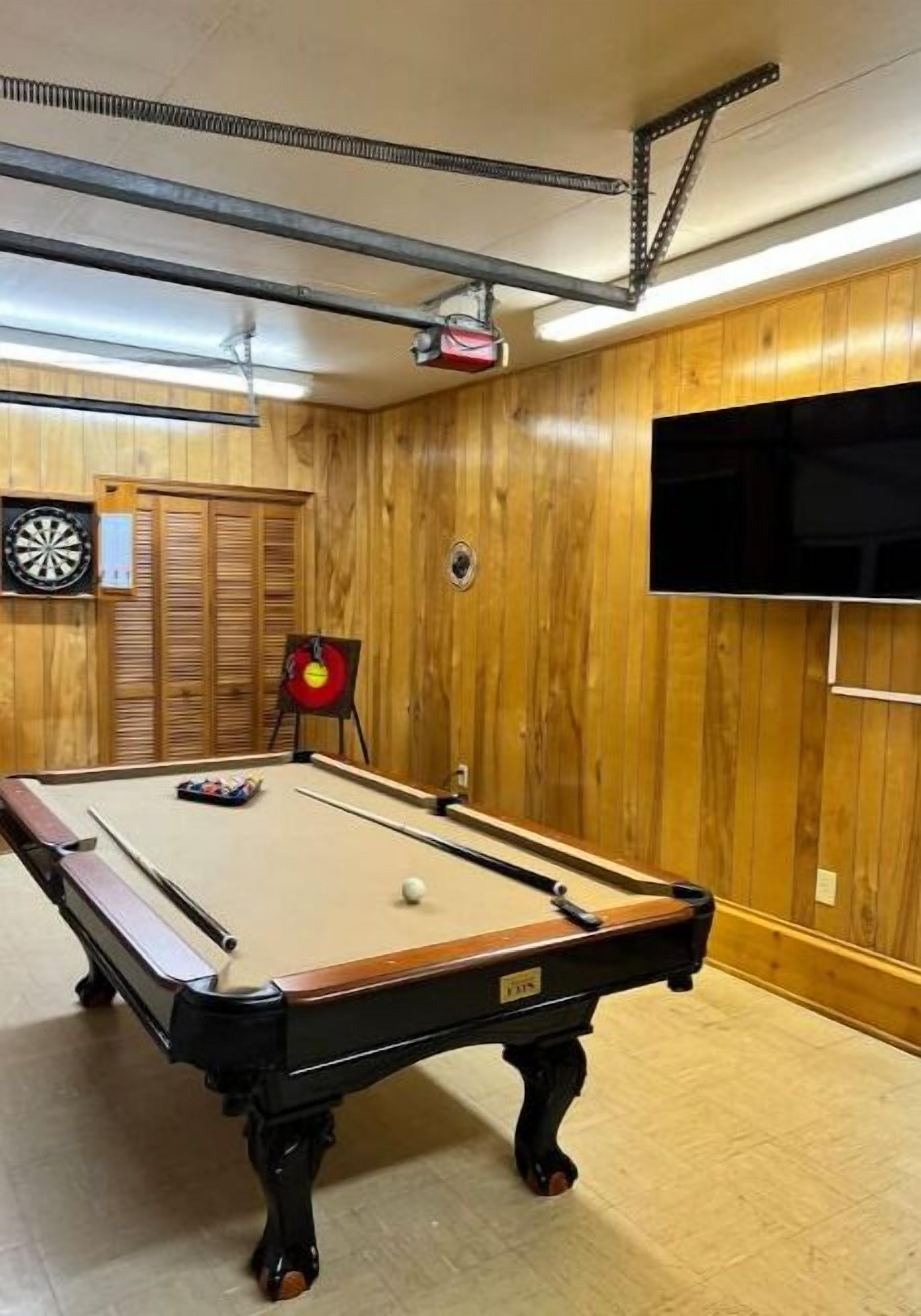 Ein Billardtisch in einem Raum mit Holzwänden und einer Dartscheibe.