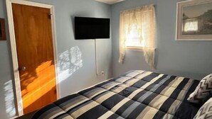 Una camera da letto con un letto, una TV a schermo piatto montata a parete, una finestra con tende e una porta.