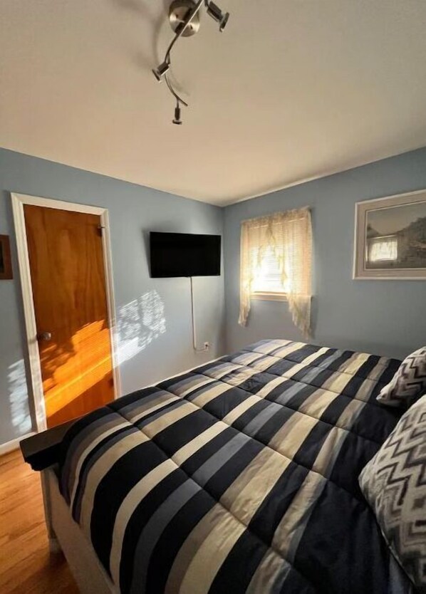 A bedroom with a bed, a flat-screen TV mounted on the wall, a window with curtains, and a door. - Cozy Cove On Sugar Creek A 2-bedroom Dream Home is located on an acre of land (Charlotte)