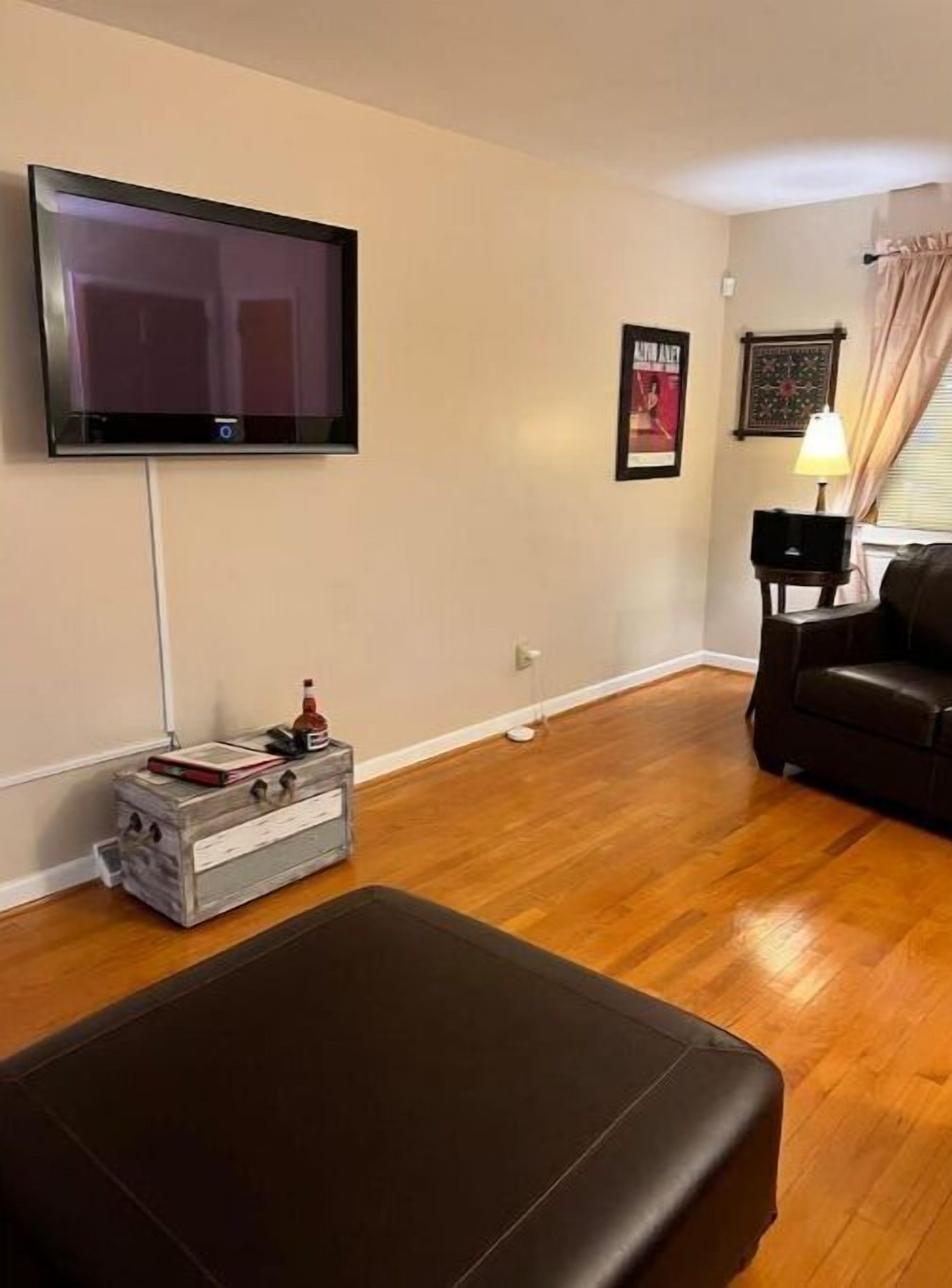 A living room with a flat-screen TV mounted on the wall, a wooden coffee table, a leather sofa, and a lamp on a side table.